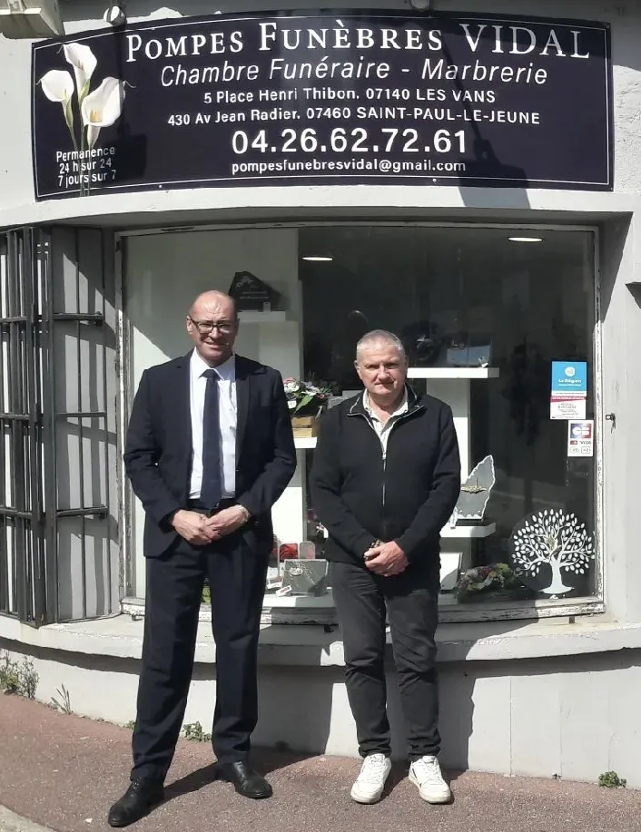 Deux hommes posant debout devant la vitrine de l'agence de Pompes Funèbres Vidal.